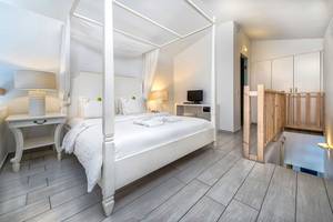 Schlafzimmer im Diamond Deluxe Hotel mit einem großen Bett, weißem Überwurf und Vorhängen.