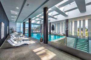 Innenpool-Loungebereich im Diamond Deluxe Hotel mit weißen Liegestühlen und Glaswänden.