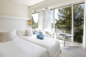 Doppelzimmer im ME Ibiza Hotel mit zwei weißen Betten, Kissen und Ausblick auf den Garten