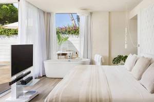 Schlafzimmer im ME Ibiza Hotel mit Badewanne, Fernseher und Pflanzen.