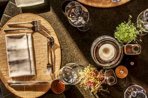 Ein Tisch im Dinarobin Beachcomber Golf Resort & Spa, mit Tellern, Besteck, Gläsern und einer Kerze dekoriert.