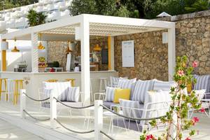 Außenbereich des Pelekas Monastery Hotels mit einer weißen Pergola, gelben Stühlen und Tischen.