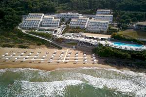 Luftaufnahme des Pelekas Klosters an der Strandpromenade mit vielen Sonnenschirmen.