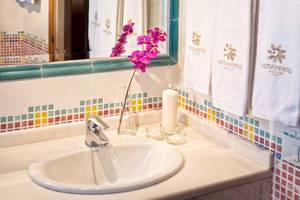 Badezimmer mit Waschbecken, Spiegel und bunten Kacheln im Sotavento Beach Club Hotel.