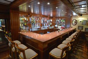 Bar im Golden Bay Beach Hotel mit Holzbar und Stühlen, voll mit Getränken.