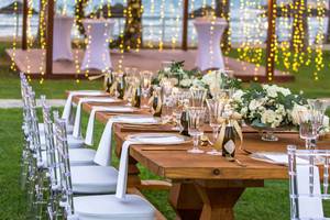 Ein Banketttisch im Freien beim Golden Bay Beach Hotel mit dekorierten Tischen und Stühlen, Gläsern, Kerzen und Blumen.