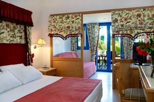 Ein Schlafzimmer im Mitsis Rinela Beach Hotel mit Doppelbett, Nachttisch, Sessel und Balkon.