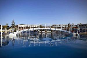 Außenpool des Mitsis Rinela Beach Hotels mit einer Brücke und Sonnenliegen.