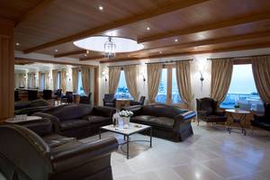 Lobby-Lounge des Mitsis Rinela Beach Hotels mit braunen Ledersofas und großen Fenstern.