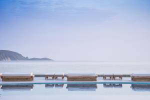 Pool-Loungebereich im Mitsis Rinela Beach Hotel mit Blick auf das Meer und Inseln.