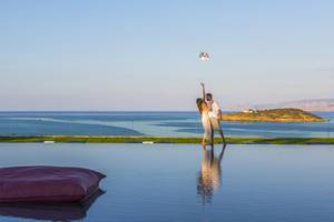 Paar im Minos Palace Hotel & Suites am Strand, das nach einem Frisbee greift, mit Blick auf das Meer.