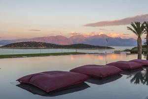 Minos Palace Hotel & Suites: Ein Swimmingpool mit roten Kissen und Blick auf eine bergige Landschaft und einen Sonnenuntergang.