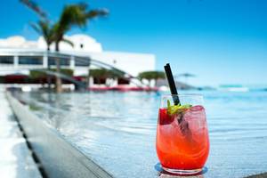 Ein roter Cocktail steht auf einer Kante am Pool im Minos Palace Hotel & Suites.