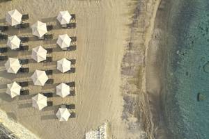 Luftaufnahme von Liegestühlen und Sonnenschirmen am Strand des Minos Palace Hotel & Suites.