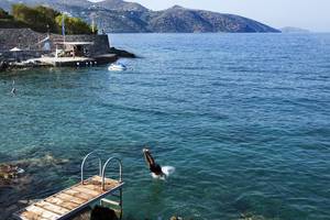 Person springt ins Meer am Minos Palace Hotel & Suites, umgeben von Klippen und Bergen.