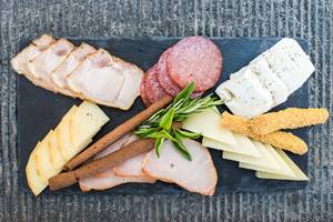 Eine Platte mit verschiedenen Fleischsorten, Käse und Kräutern auf einem schwarzen Untergrund.