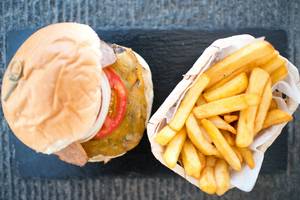 Ein Burger mit Tomatenscheibe und Pommes Frites in Papierschalen auf einem Tisch