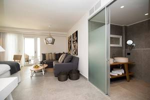 Innenansicht eines Zimmers im Insula Alba Resort & Spa mit Bett, Sofa, Tisch und Badezimmer.