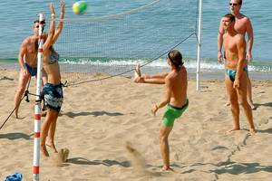 Gruppe junger Männer und Frauen spielt Volleyball am Strand in der Nähe des Wassers