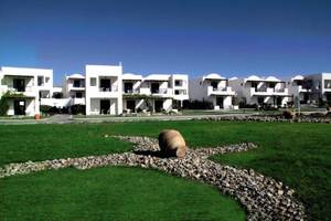 Außenansicht des Atlantica Beach Resort Kos mit weißen Gebäuden und grüner Rasenfläche.