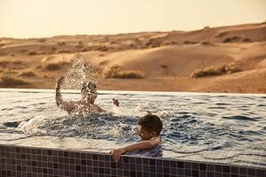 Zwei Kinder schwimmen und spielen in einem Pool vor einer Wüstenlandschaft im Ritz-Carlton Ras Al Khaimah, Al Wadi Desert.