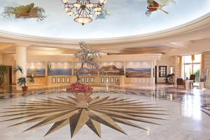 Lobby des Lindos Princess Beach Hotels mit einer großen Lichtkrone, einer zentralen Pflanzenvase und einer gemusterten Decke.