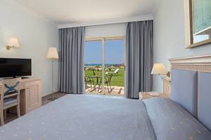Zimmer im Lindos Princess Beach Hotel mit Meerblick, Bett, Schreibtisch, Fernseher und Glastür.