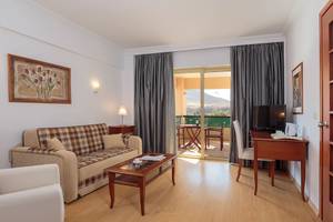 Innenansicht eines Zimmers im Lindos Princess Beach Hotel mit einem Sofa, einem Tisch und einem Fernseher.