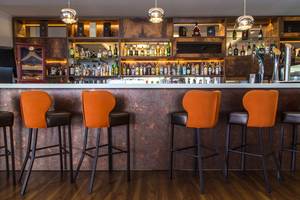 Innenansicht der Bar im Lordos Beach Hotel mit orangefarbenen Stühlen und einer großen Auswahl an Getränken.