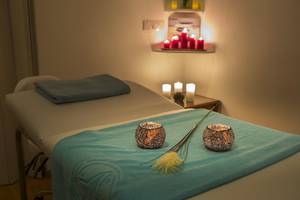 Massageraum im Lordos Beach Hotel mit blauen Laken, Kerzen und Pflanzen.