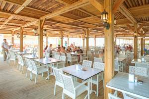 Terrasse des Side Orange Palace Hotels mit Gästen an Tischen unter Holzsäulen.