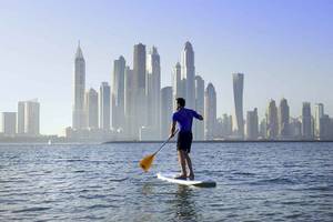 Mann auf Paddelboard mit Blick auf die Skyline von Dubai vor dem Sofitel Dubai The Palm
