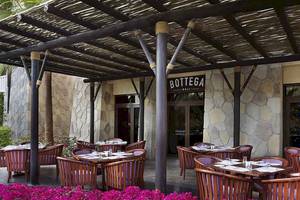 Außenbereich des Restaurants Bottega Deli im Sofitel Dubai The Palm mit holzigen Tischen und Stühlen unter einem Dach.