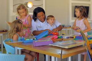 Eine Mitarbeiterin des Trou aux Biches Beachcomber Golf Resort & Spa hilft Kindern beim Basteln an einem Tisch.