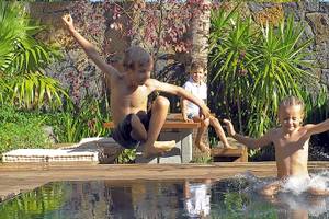 Drei Kinder springen in einen Pool im Garten des Trou aux Biches Beachcomber Golf Resort & Spa.
