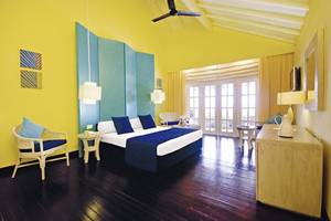 Hotelzimmer im Adaaran Select Meedhupparu mit gelben Wänden, blauer Bettwäsche und einem offenen Fenster.