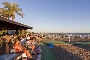 Strandterrasse im Miracle Resort mit vielen Gästen, Sonnenschirmen und einer Aussicht auf das Meer.