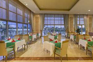 Restaurant im Miracle Resort mit großen Fenstern und grünen Tischdecken.
