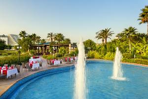 Außenbereich des Miracle Resorts mit Swimmingpool, Tischen und Palmen.