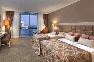 Doppelzimmer im Miracle Resort mit Balkon und Meerblick, zwei Betten, Schreibtisch, Fernseher und großem Fenster.