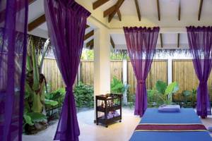 Spa-Behandlungsraum im OBLU NATURE Helengeli mit blauer Bettdecke, Holzstuhl und lila Vorhängen.