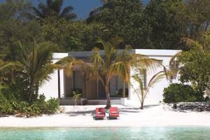 Weißes Hotel OBLU NATURE Helengeli am Strand mit zwei roten Sonnenliegen und Palmen