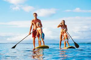 Eine Familie auf Stand-Up-Paddle-Brettern im Wasser, mit klarem Himmel im Hintergrund.