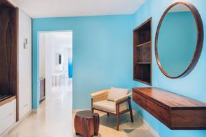 Innenansicht der Suite im Coral Level at Iberostar Selection Cancun mit blauen Wänden, einem Holzstuhl und einem Spiegel.