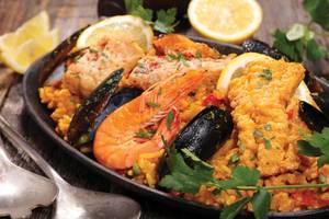 Eine traditionelle spanische Paella mit Garnelen, Muscheln und Zitrone serviert auf einem Holztisch.