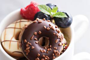 Ein weißer Becher mit Schokoladen-Donuts, gefüllt mit verschiedenen Beeren und Minzblättern.