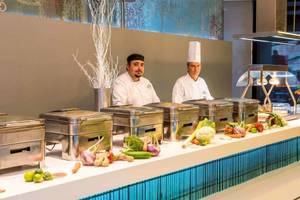 Zwei Köche in der Küche von AX The Palace, das Buffet ist voller Gemüse und Früchte.