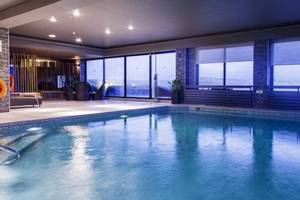 Innenpool des AX The Palace Hotels mit großen Fenstern und Loungebereich.