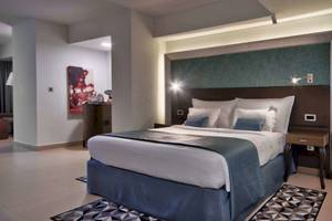 Innenansicht eines Hotelzimmers im AX The Palace mit einem großen Bett, Dekor und Nachttischen.