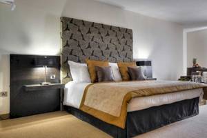 Schlafzimmer im AX The Palace Hotel mit großem Bett, dekorativen Kissen und Nachttischen.